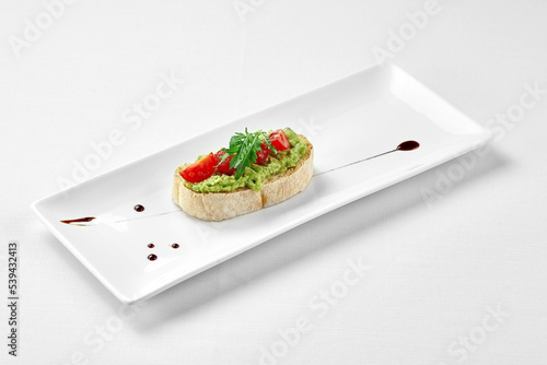 Bruschetta with avocado and tomatoes in a white plate on a white background. Close-up, selective focus