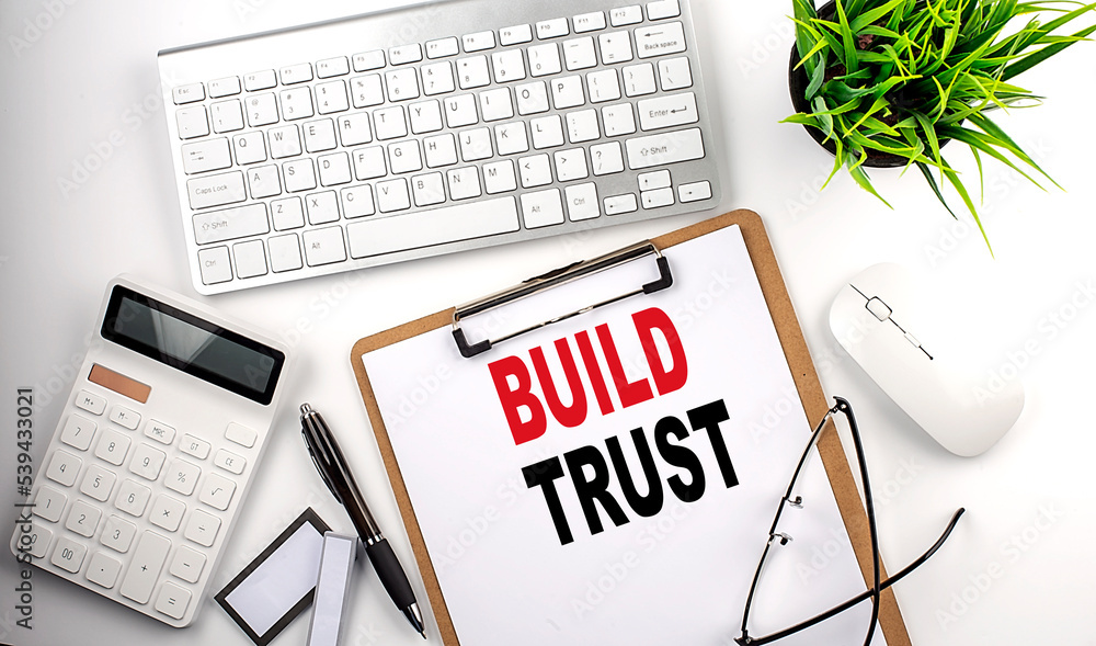 Business concept.Text BUILD TRUST on paper clipboard with,pencil,glasses, keyboard and calculator on white background. Business concept.Text BUILD TRUST on paper clipboard with,pencil,glasses, keyboard and calculator on white background.