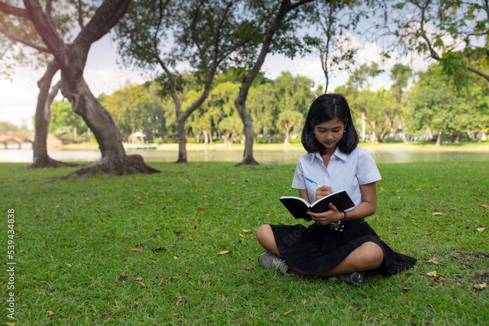 Beautiful portrait photo of a young beautiful asian female thai lady in university student uniform holding a book in a park Beautiful portrait photo of a young beautiful asian female thai lady in university student uniform holding a book in a park