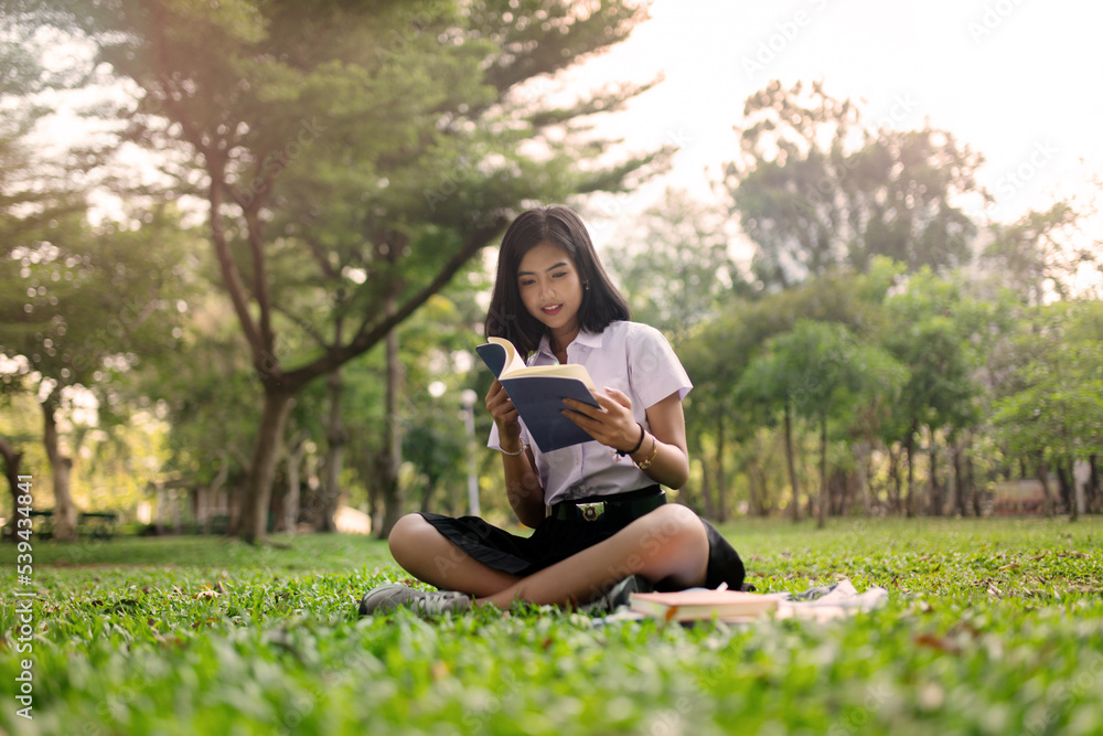 Beautiful portrait photo of a young beautiful asian female thai lady in university student uniform holding a book in a park