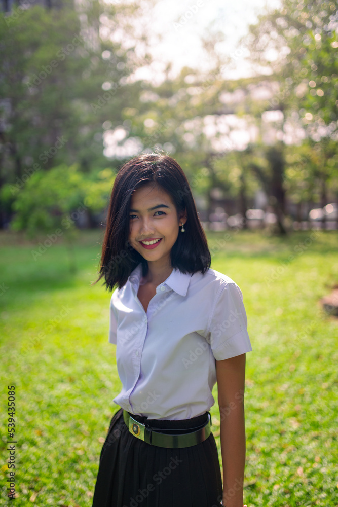 Portrait photo of a young asian beautiful lady in thai university student uniform smile happily in a park with nice sunlight from the back Portrait photo of a young asian beautiful lady in thai university student uniform smile happily in a park with nice sunlight from the back