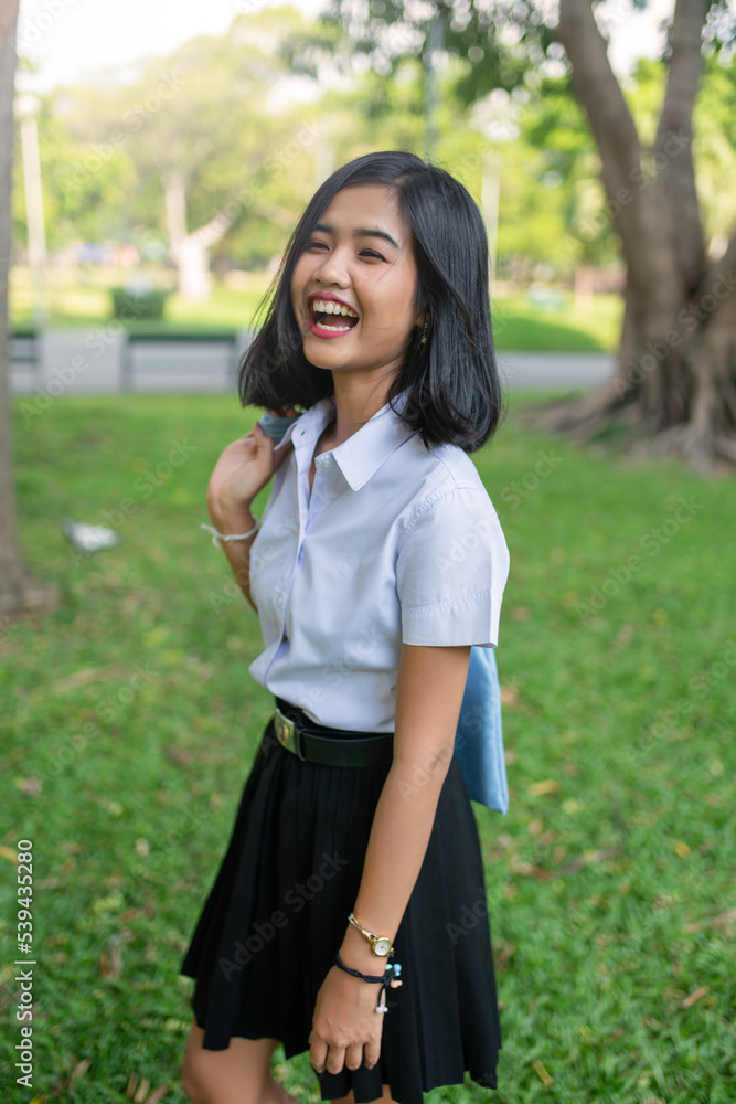 Portrait photo of a young asian beautiful lady in thai university student uniform smile happily with a recycle bag in a park Portrait photo of a young asian beautiful lady in thai university student uniform smile happily with a recycle bag in a park