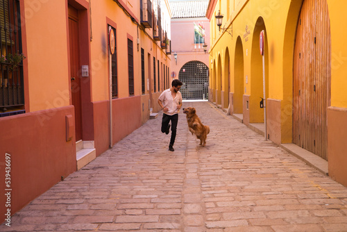 handsome  young Hispanic man with his brown golden retriever dog  running through the streets of a European city while having fun. Concept pets  animals  dogs  pet love  golden retriever.