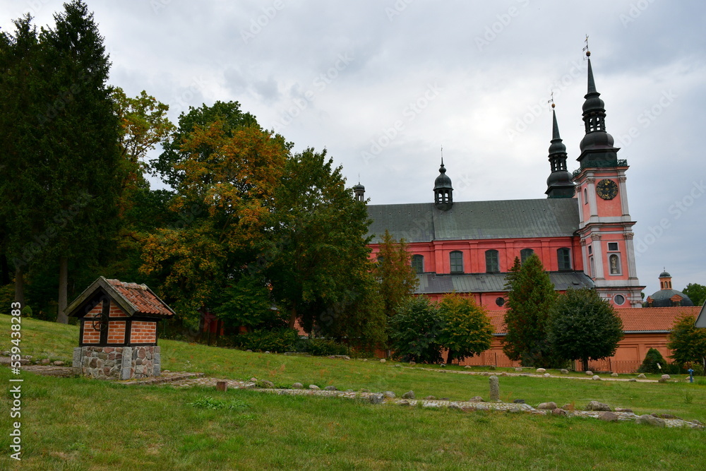 A close up on a small well with a metal wheel made out of stones, boulders, red bricks, and tiles, located next to some stone steps, old manor and a church spotted on a gloomy autumn day in Poland A close up on a small well with a metal wheel made out of stones, boulders, red bricks, and tiles, located next to some stone steps, old manor and a church spotted on a gloomy autumn day in Poland