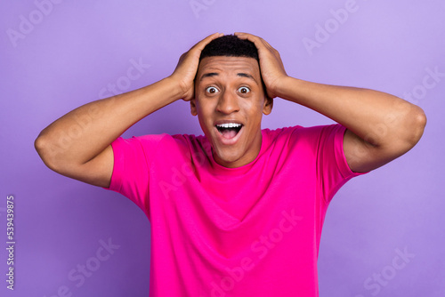 Portrait of handsome impressed astonished man with fade hairstyle dressed pink t-shirt hands on head isolated on violet color background
