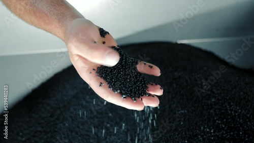 A man collects rubber granules with his hand, close-up. Raw material for production of rubber products. photo