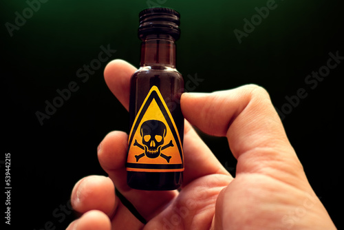 Fotografie hand holding a small bottle of poison with a yellow toxic sign represented by a