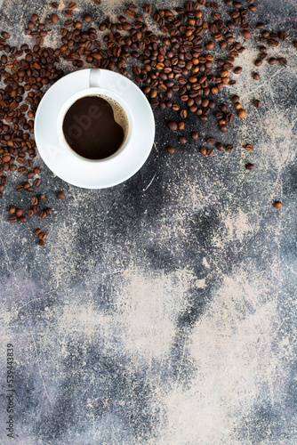white cup of fresh brewed coffee and much roasted coffee beans on an old background with chocolate