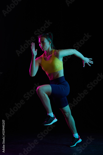 Running technique. Professional female jogger running isolated on dark background in neon light. Sport, fitness, speed and energy concept. © master1305