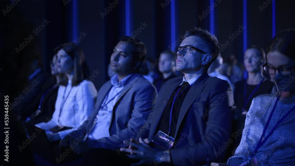 Young Man Sitting in a Crowded Audience at a Business Conference. Corporate Delegate Watching Inspirational Entrepreneurship Presentation About Developing Markets and Financial Opportunities. Young Man Sitting in a Crowded Audience at a Business Conference. Corporate Delegate Watching Inspirational Entrepreneurship Presentation About Developing Markets and Financial Opportunities.