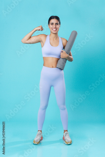 Young woman feeling determined and achieving a goal, holding a yoga mat; pastel colors, teal studio background