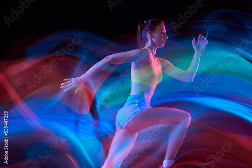 Glow. Professional female athlete, runner in motion over dark background in mixed neon light. Art, beauty, sport, cyberpunk concept © master1305