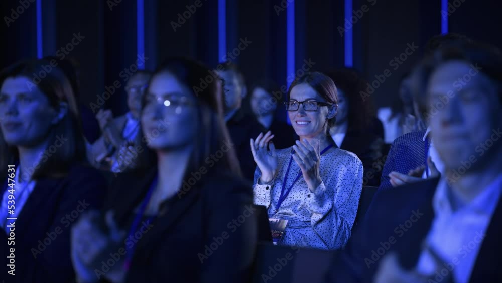 Beautiful Female Sitting in a Dark Crowded Auditorium at a Conference. Young Woman Clapping After a Successful Keynote Presentation. Specialist Inspired by Latest Technology. Slow Motion Footage. Beautiful Female Sitting in a Dark Crowded Auditorium at a Conference. Young Woman Clapping After a Successful Keynote Presentation. Specialist Inspired by Latest Technology. Slow Motion Footage.