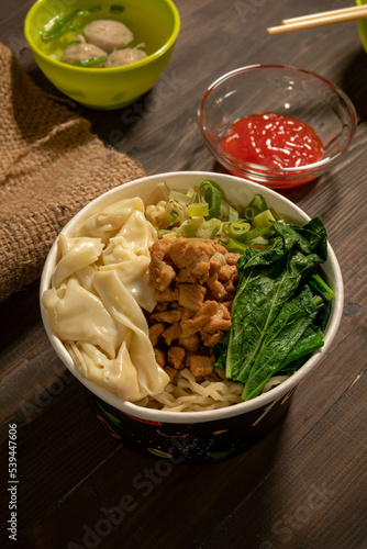 Chicken noodles in white bowl and wooden chopsticks on natural background with chicken pieces, green mustard greens, meatballs, boiled dumplings, sauce. Indonesian Chicken Noodles photo