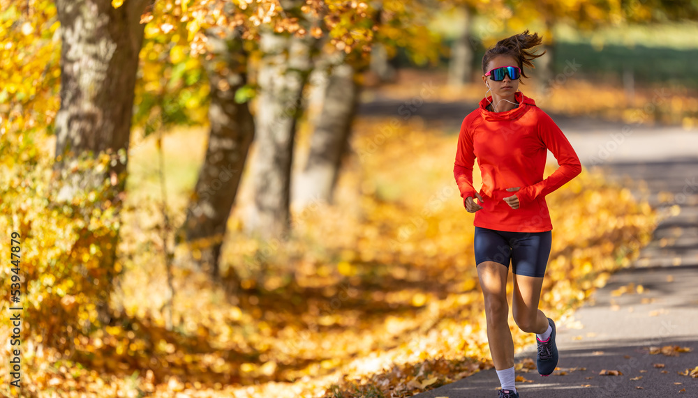 Young female athlete in sportswear runs in the park during warm indian summer Young female athlete in sportswear runs in the park during warm indian summer