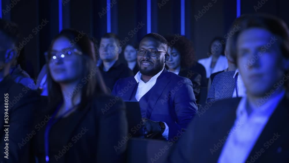 Black Man Sitting in a Crowded Audience at a Business Conference. Corporate Delegate Entertained by a Joke, While Listening to an Inspirational Entrepreneurship Presentation About Developing Markets. Black Man Sitting in a Crowded Audience at a Business Conference. Corporate Delegate Entertained by a Joke, While Listening to an Inspirational Entrepreneurship Presentation About Developing Markets.
