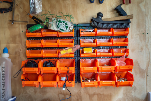 Wall hanging, tool shed, storage organiser plastic shelf rack. Orange colour on wooden wall.