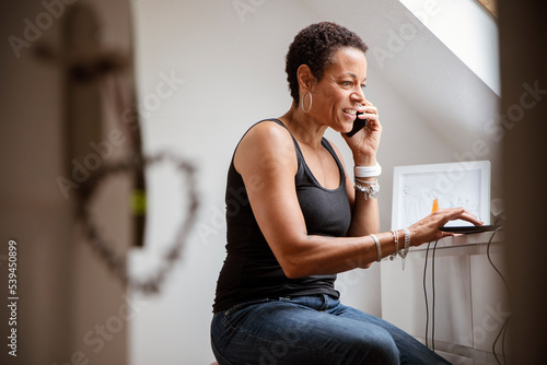 Mature woman talking on smart phone in home office