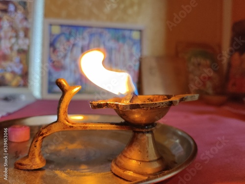 Picture of Diya lamp. Diwali Celebration. Oil lamp made from clay or mud with a cotton wick dipped in ghee. Lit diya lamp. Sculpture of Gods and goddess in background
 photo