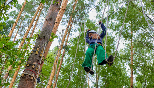 Child wins by climbing high rope, wearing mountain helmet and protective gear. Rope adventure park. The concept of sport, healthy lifestyle, strength, training.