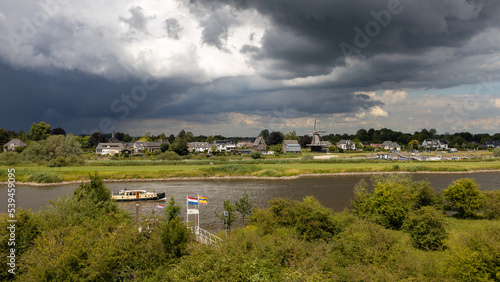Veessen, Netherlands - July 3 2022: Typical dutch landscape with a boat sailing on river IJssel nearby the village of Veessen.