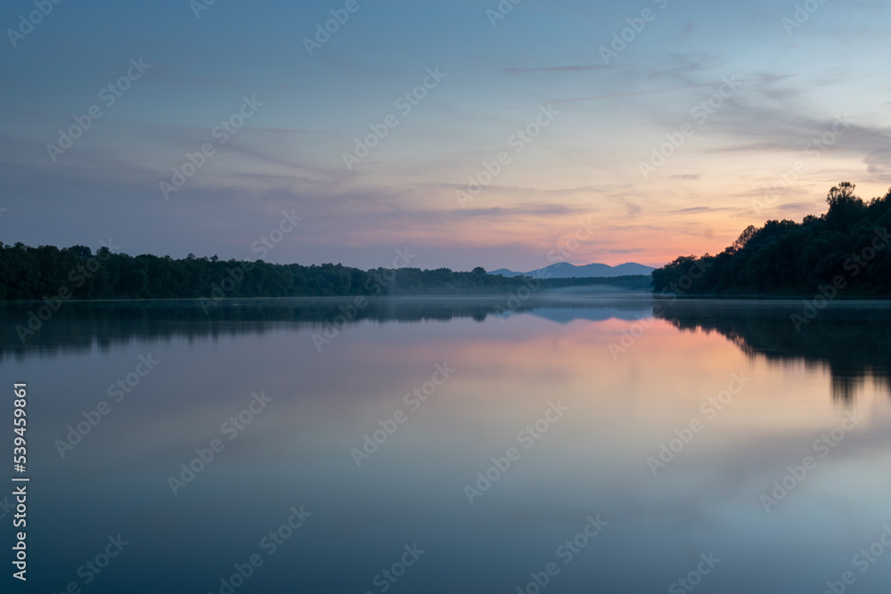 Landscape of river with fog on water surface and distant mountain at twilight, symmetric reflection and pastel colors