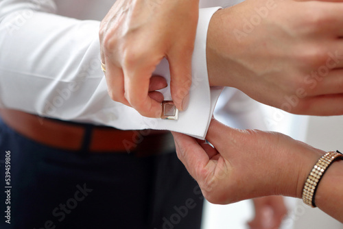 The cufflink for the shirt is put on by a mother for her son on his wedding day