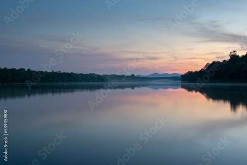 Fototapeta Naklejka Na Ścianę i Meble -  Landscape of river with fog on water surface and distant mountain at twilight, symmetric reflection and pastel colors