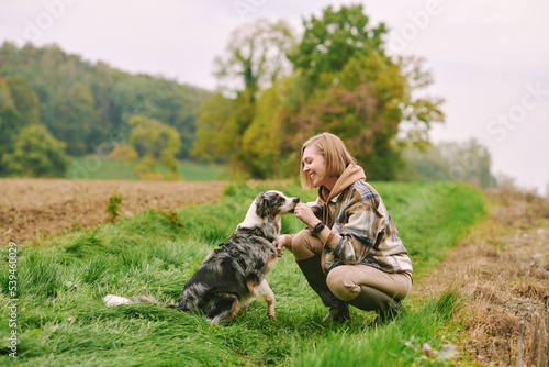 Outdoor portrait of beautiful young woman playing with australian shepherd dog