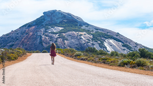 long-haired girl in a dress walks along a road in the middle of nowhere in western australia overlooking a massive mountain; australian outback