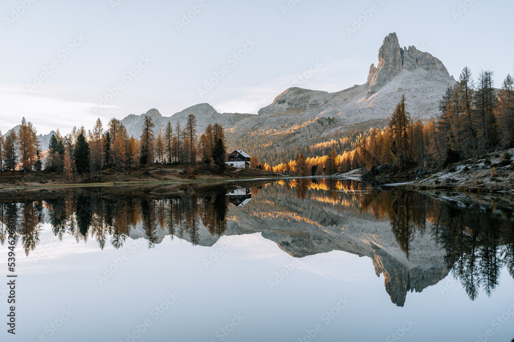 Erste Sonnenstrahlen am Lake Fedare / Lago di Federa in den Belluner Dolomiten zum Sonnenaufgang. Es ist Herbst und der Wald am See leuchtet gelb. Sonnenaufgang Dolomiten 1
