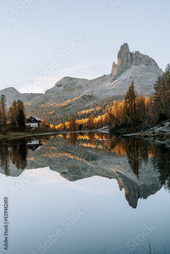 Erste Sonnenstrahlen am Lake Fedare / Lago di Federa in den Belluner Dolomiten zum Sonnenaufgang. Es ist Herbst und der Wald am See leuchtet gelb. Sonnenaufgang Dolomiten 2