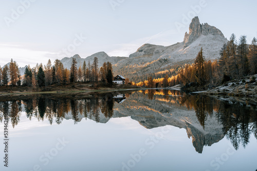 Erste Sonnenstrahlen am Lake Fedare / Lago di Federa in den Belluner Dolomiten zum Sonnenaufgang. Es ist Herbst und der Wald am See leuchtet gelb. Sonnenaufgang Dolomiten 1