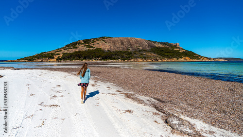 a long-haired girl in a dress walks on a paradise beach in western australia; a beach with turquoise water, white sand and massive mountains in the background