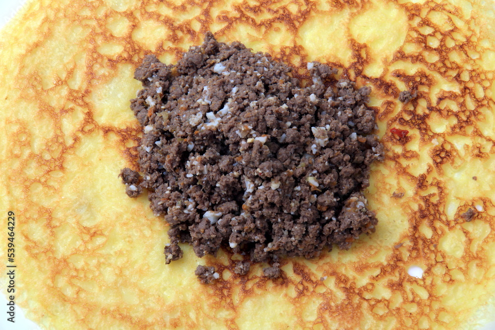 Minced meat filling on a large thin pancake. Making a pancake filled with meat or heart