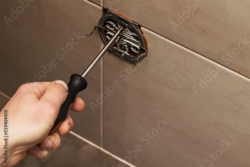 Repairman screws Socket by Screwdriver on Tiles Wall. Service Repair at Home Concept