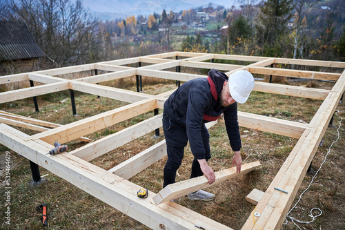 Men workers building wooden frame house on pile foundation. Carpenters installing wooden truss for timber framing. Carpentry concept.