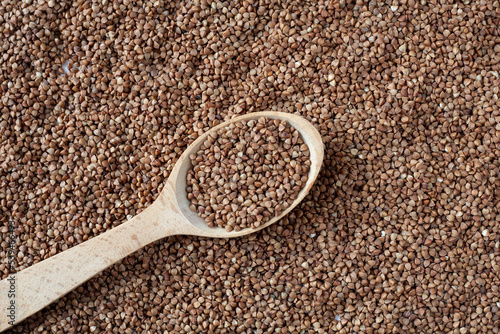 On the table is a wooden spoon with buckwheat grains. Around it are buckwheat grains.