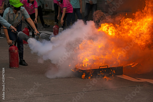 Two young female trainees use carbon dioxide fire extinguishers to extinguish a fire caused by burning gasoline in a tray with a trainer supervising the training. Event of fire fighting training.