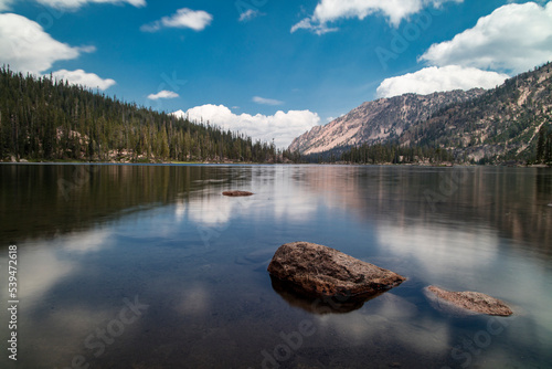 Imogene Lake  a large alpine lake in Idaho s Sawtooth Mountains and within the Sawtooth Wilderness. Seen on a summer day with blue sky and white clouds reflected in the water s surface.