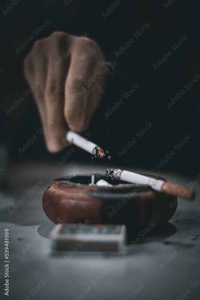 Vertical shot of a hand in a dark background flicking cigarette ash
