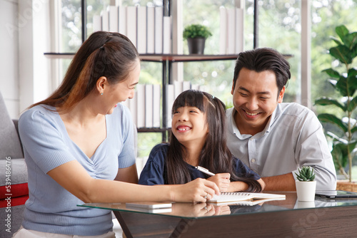 Children education and home school concept : Young asian father and mother see little daughters' study. Excited smiling small child girl enjoying learning and writing with pleasant dad and mom at home