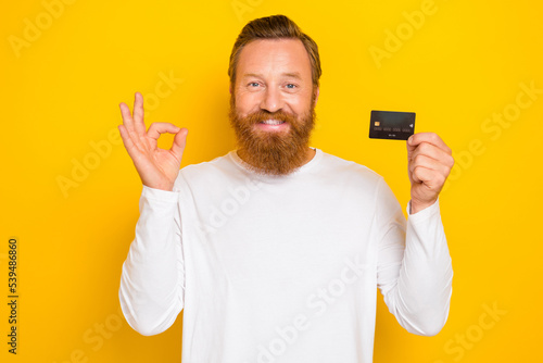 Photo of positive stylish man trendy outfit get arm hold plastic bank card show okey symbol recommend isolated on yellow color background