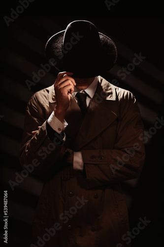 A dark silhouette of a man from the face in a coat and hat. A dramatic portrait in the style of detective films and spy books of the 1950s and 60s.