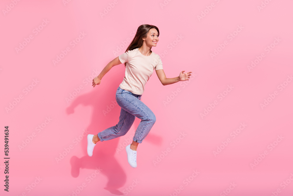 Full length photo of excited cute girl dressed beige t-shirt jumping high hurrying empty space isolated pink color background