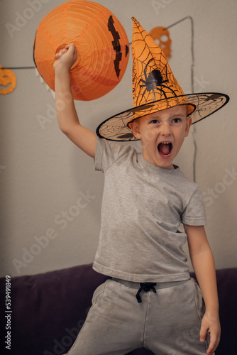Boy with funny face in orange hat holding artificial pumpkin, halloween concept. High quality photo