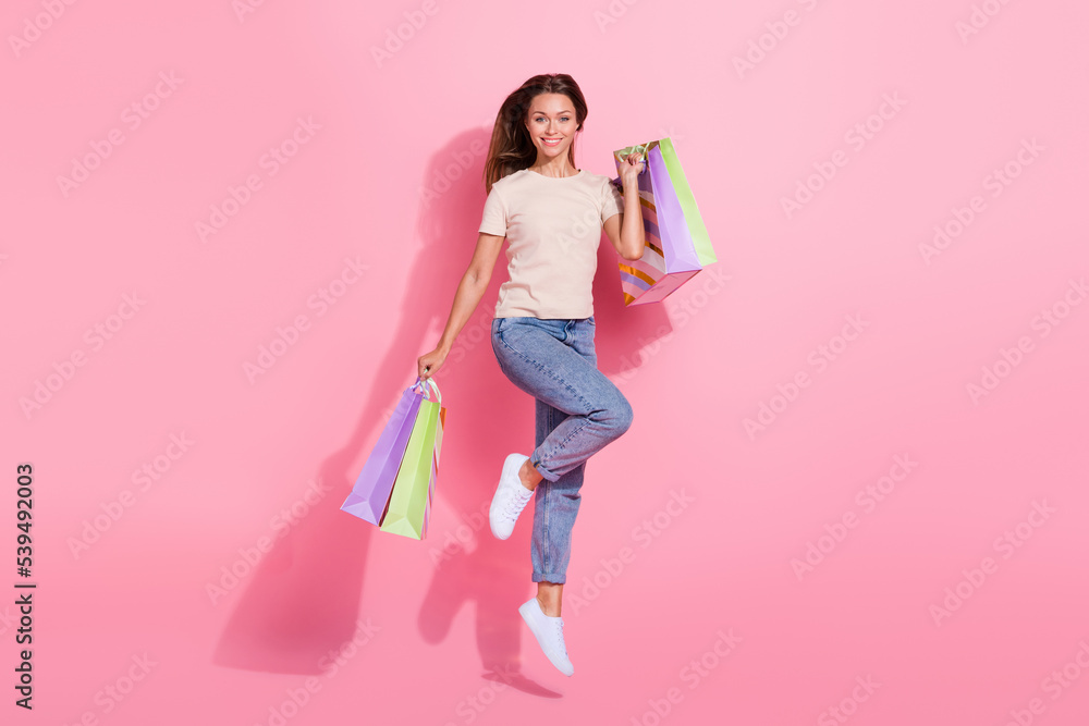 Full length photo of sweet adorable girl dressed beige t-shirt jumping high rising bargains isolated pink color background Full length photo of sweet adorable girl dressed beige t-shirt jumping high rising bargains isolated pink color background
