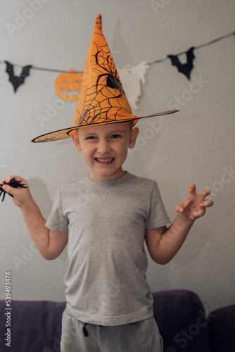 Boy in orange halloween hat with spider making funny and scary faces, halloween concept. High quality photo