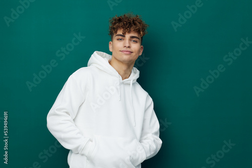 a cute  funny  joyful man stands on a green background in a white hoodie and looks pleasantly into the camera. Horizontal studio photo for inserting an advertising layout