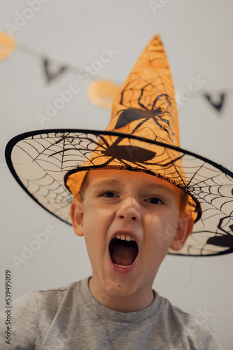 Boy in orange halloween hat with spider making funny and scary faces, halloween concept. High quality photo